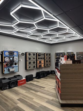 Black and brown customized golf cart with large tires, speakers, and cushioned seats in a showroom.