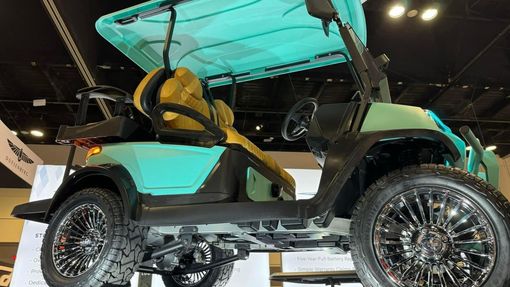 Teal and black golf cart with yellow seats and chrome wheels, indoors.