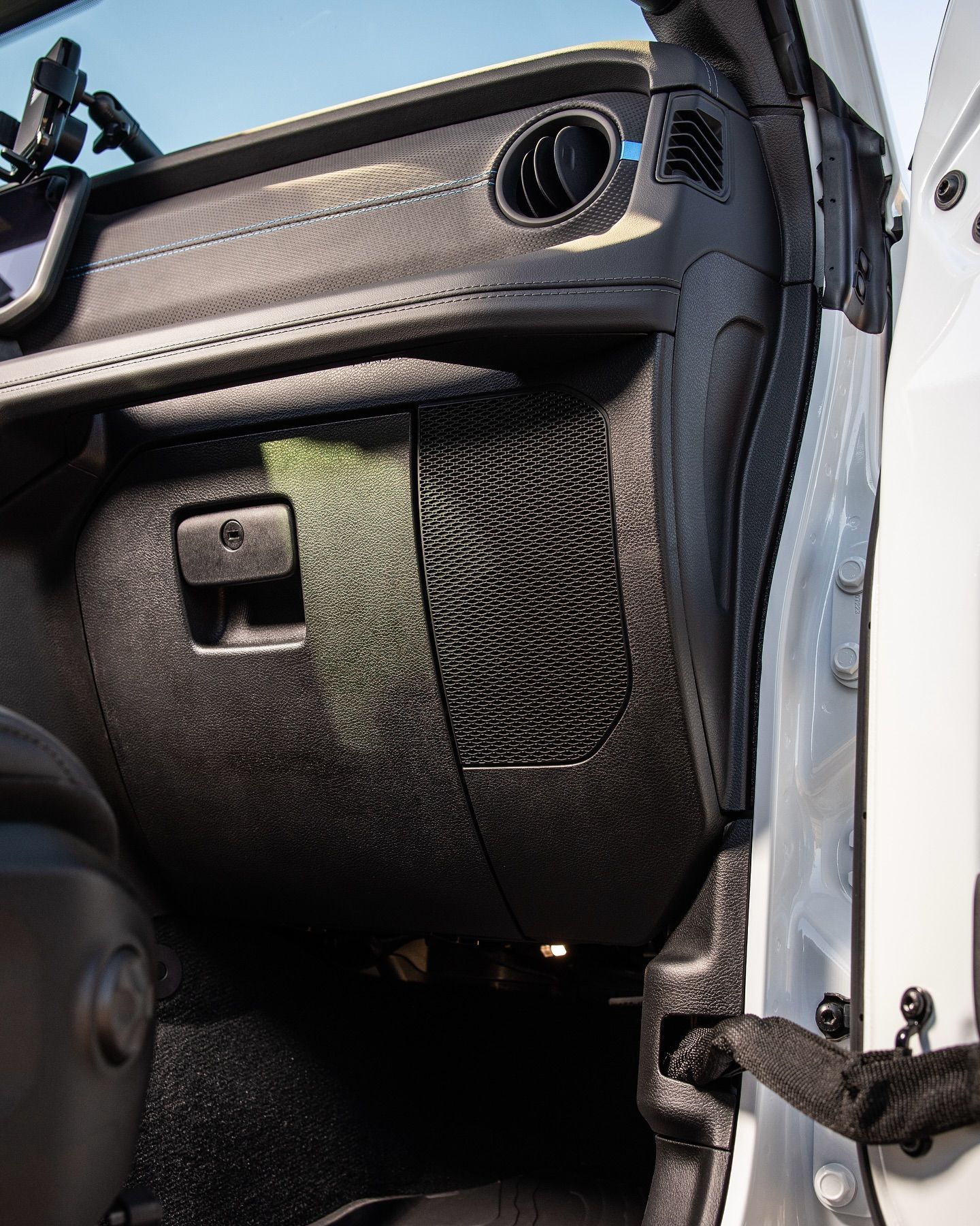 Black dashboard interior of a vehicle with an open door.  Visible speaker, air vent, and glove compartment.