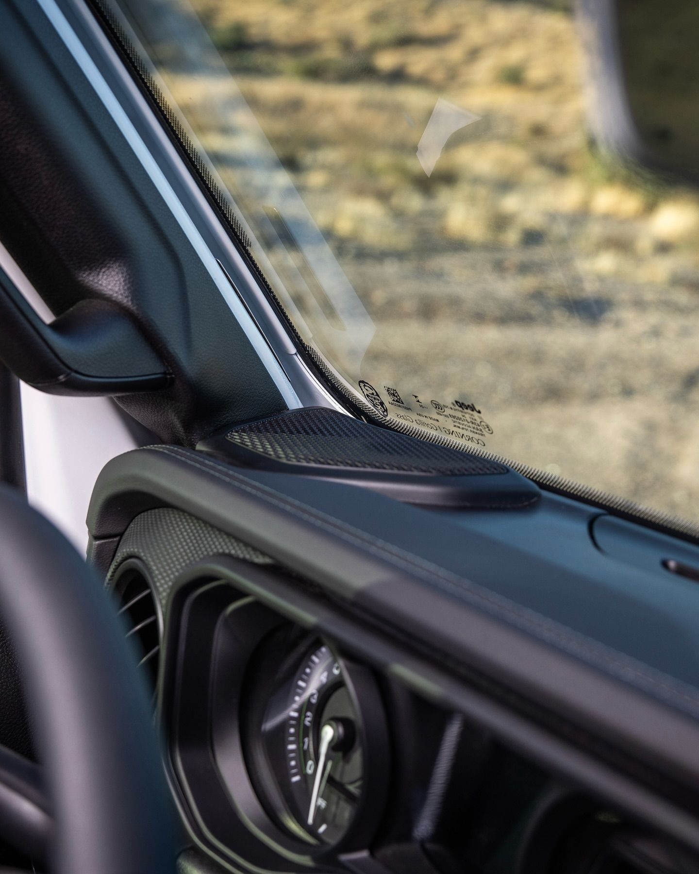 Interior dashboard view of a vehicle, with speaker, gauge, and windshield.
