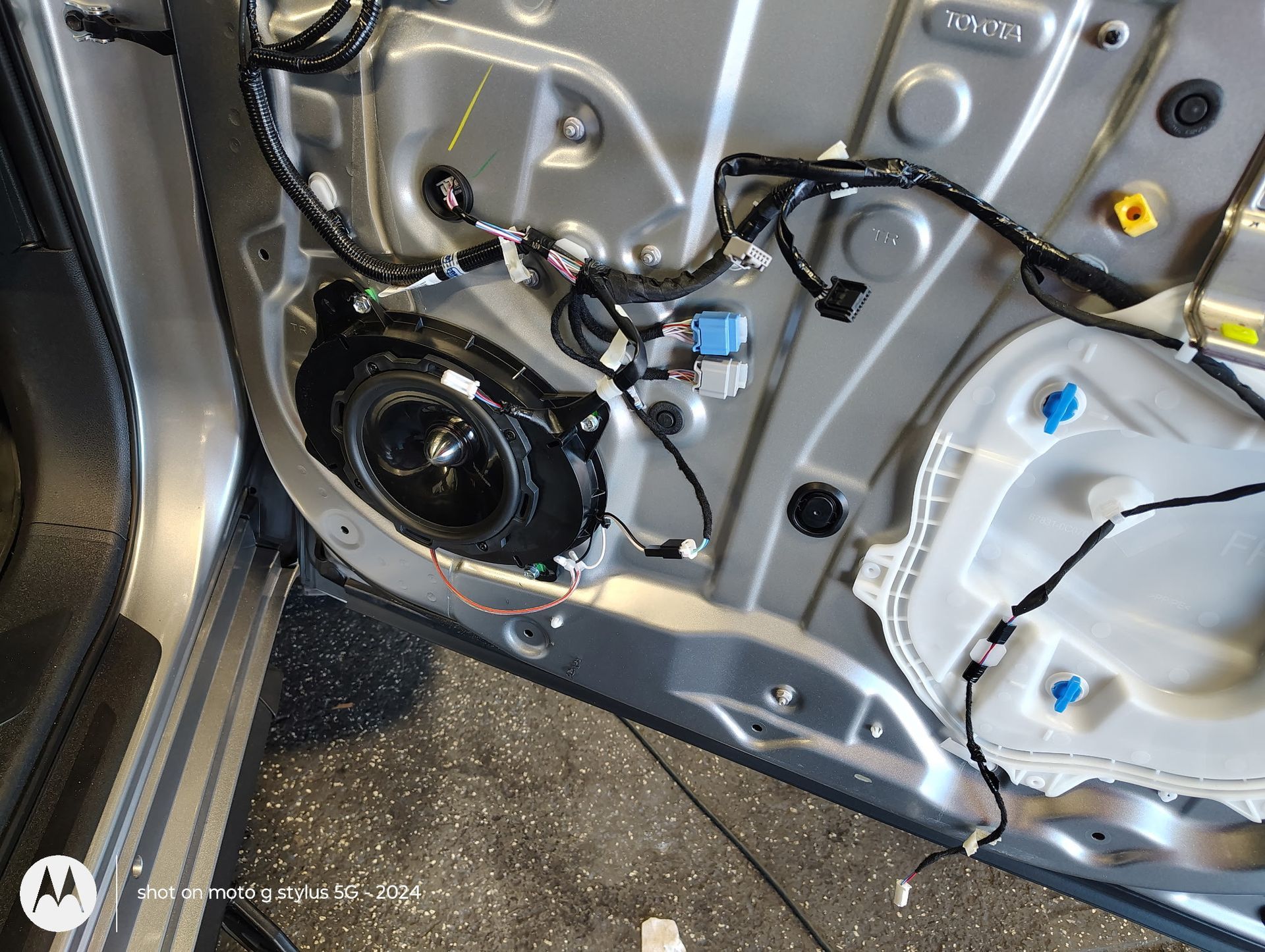 Car door interior with speaker, wires, and components visible. Silver metal panel.