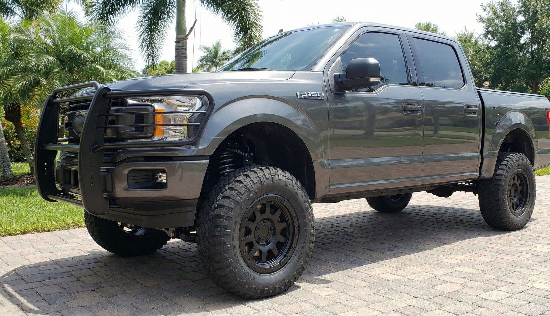 Silver car being lifted by a red floor jack, likely for tire change, indoors on tile.