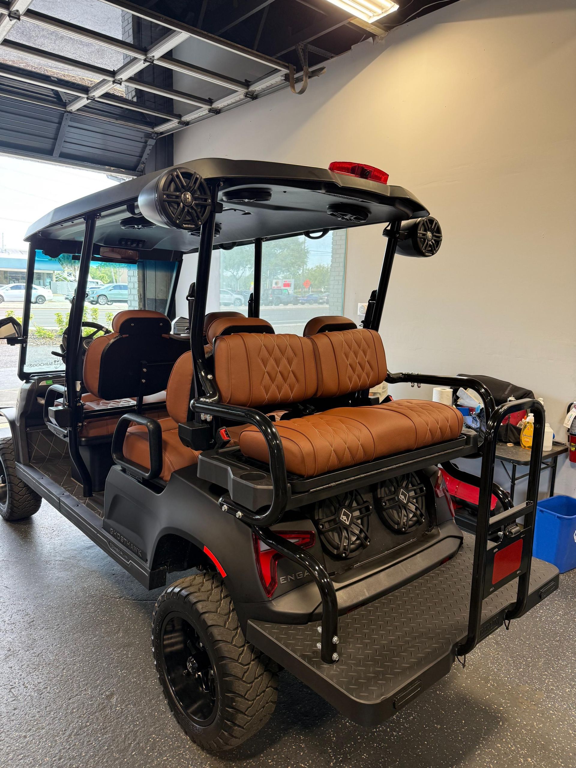 Black golf cart with brown quilted seats and speakers, parked indoors.