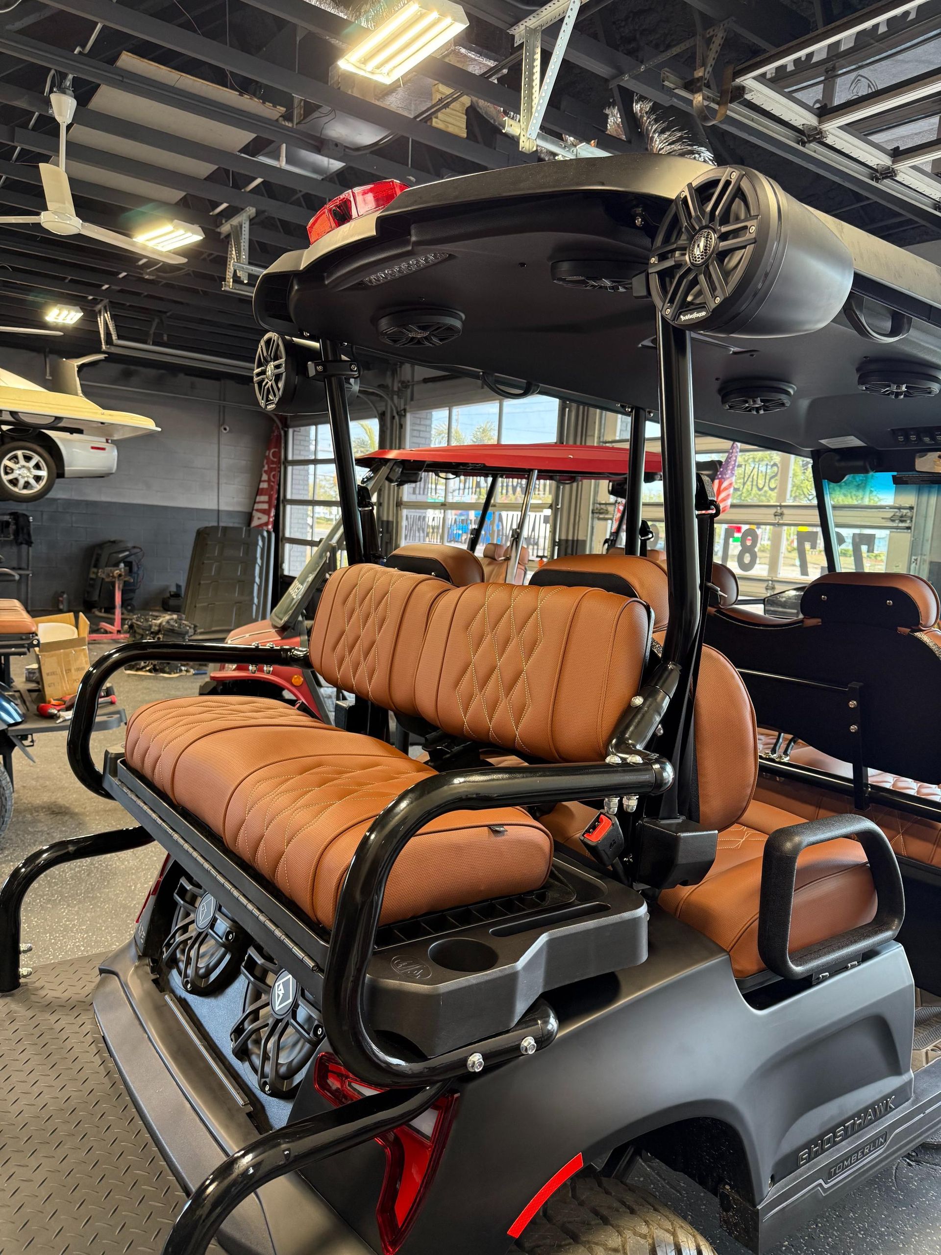 Custom golf cart with brown quilted seats, black frame, and speakers on the roof in a garage.