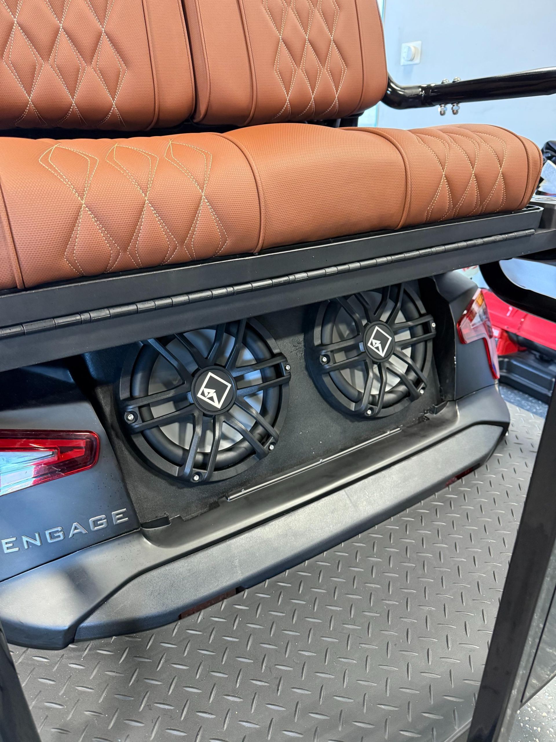 Two black speakers built into the back of a gray golf cart, below a brown quilted seat.