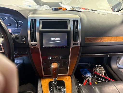 Close-up of a car's interior featuring black leather shift knob, red off-road controls, and a dial with logo.