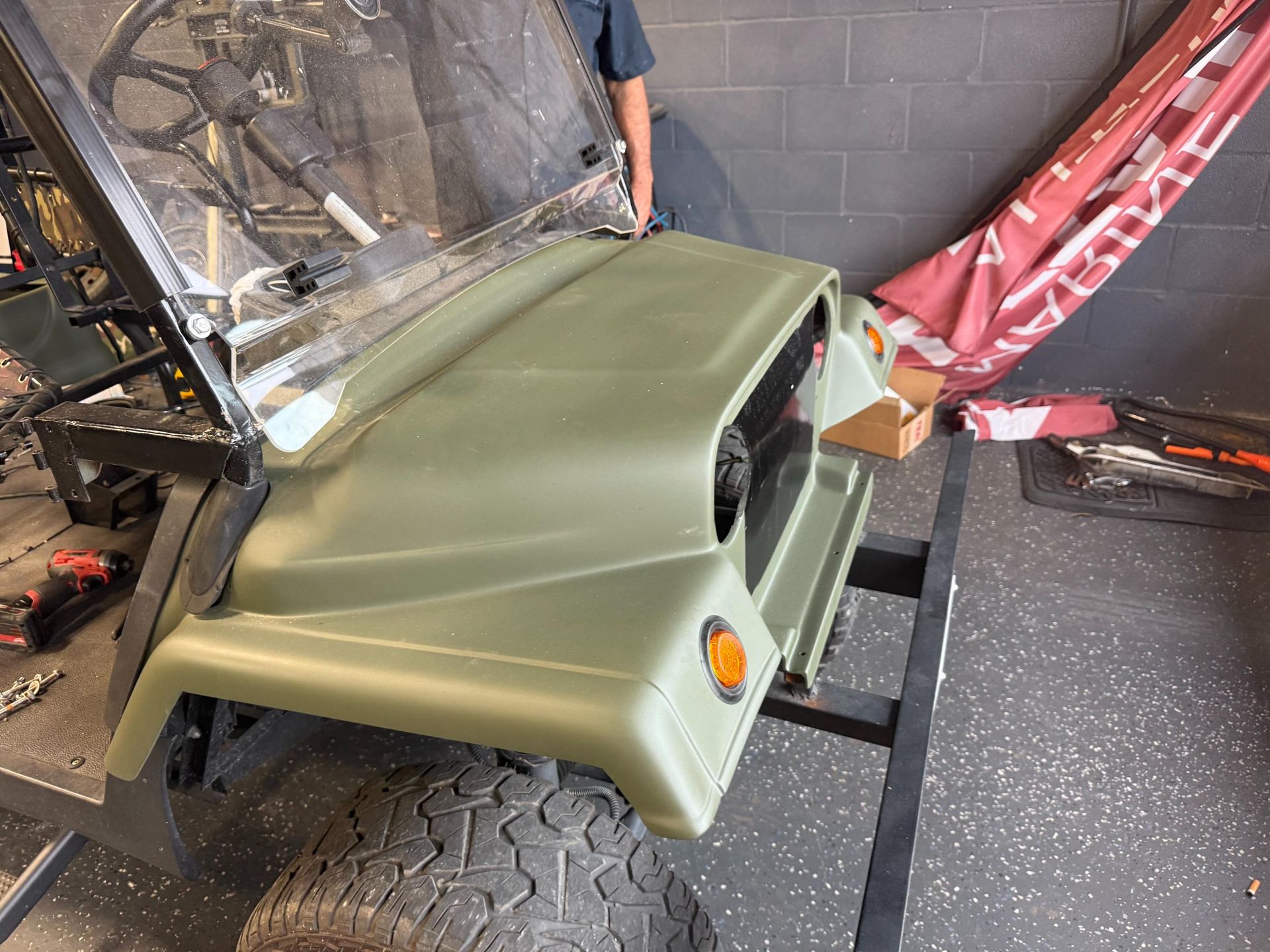 Green golf cart's front end, raised windshield, in garage setting.