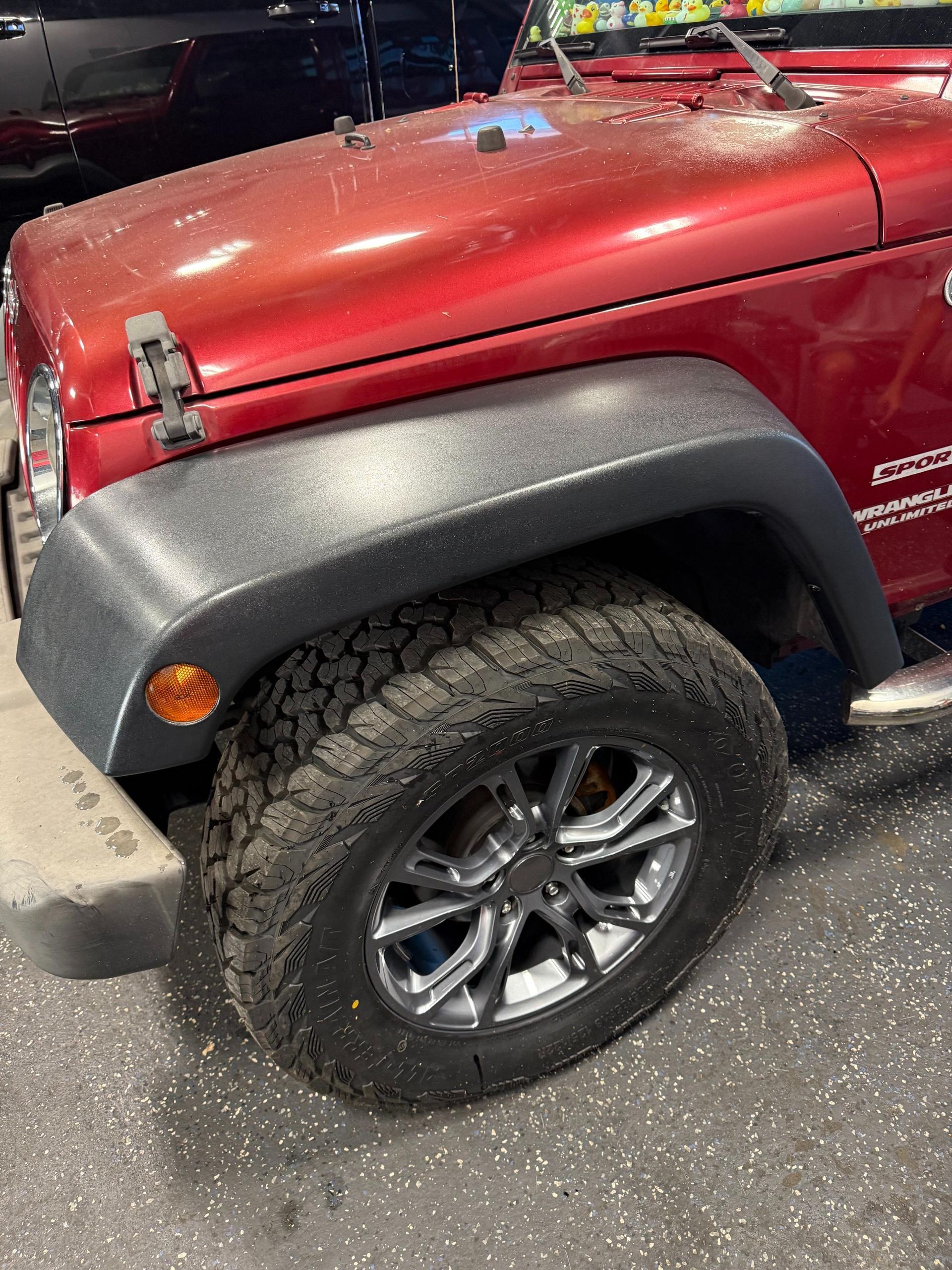 Red Jeep Wrangler with black fender, off-road tire, and chrome rim.