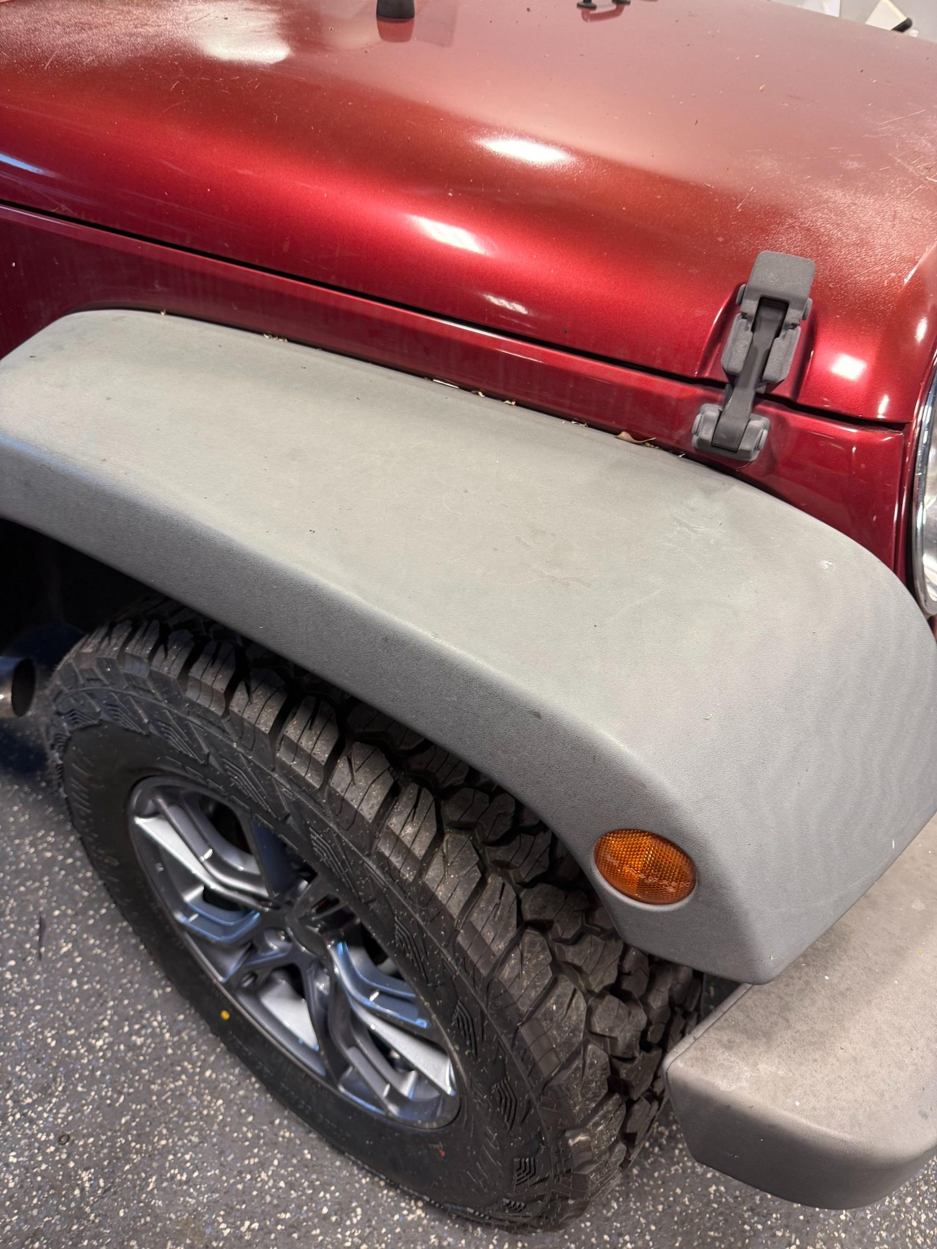Red Jeep Wrangler's front, showing fender, tire, and hood. Gray fender with amber side marker light.
