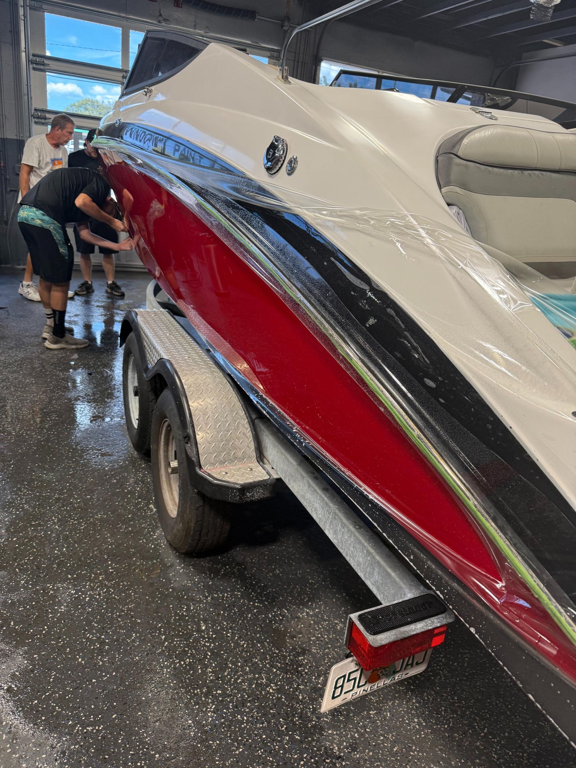 People washing a red and white boat on a trailer in a garage.