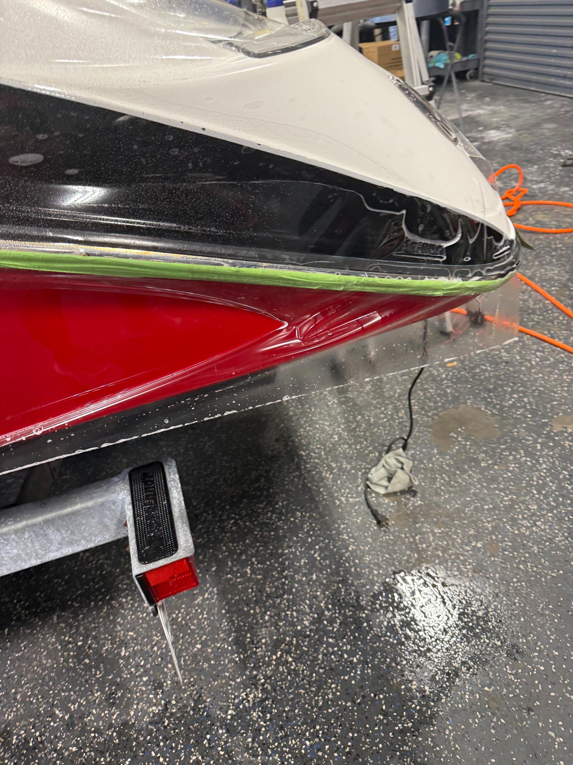 Boat hull, red and black paint, white top, being worked on in a shop, trailer visible.