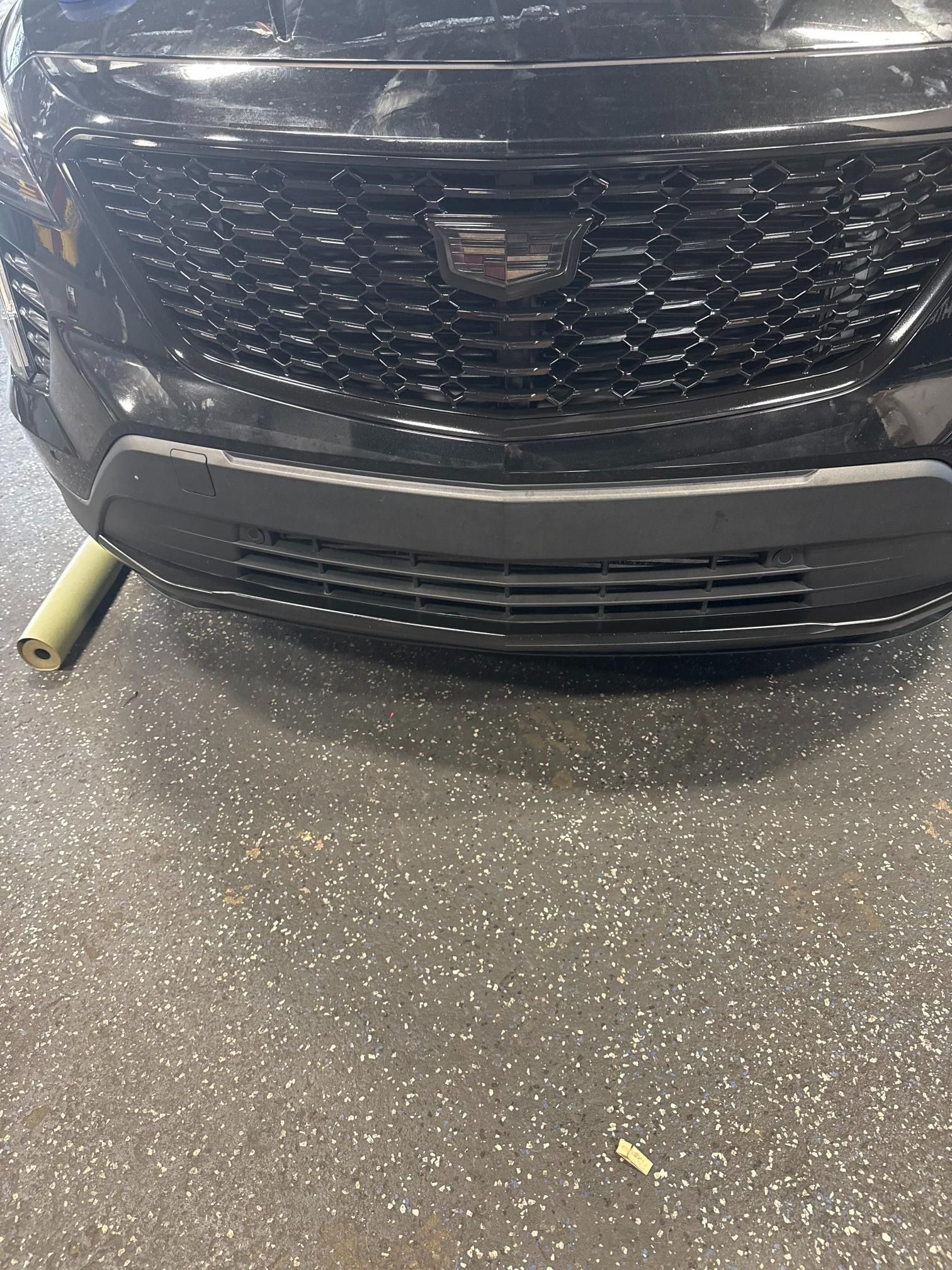 Black Cadillac SUV front with grill and bumper, resting on a workshop floor.