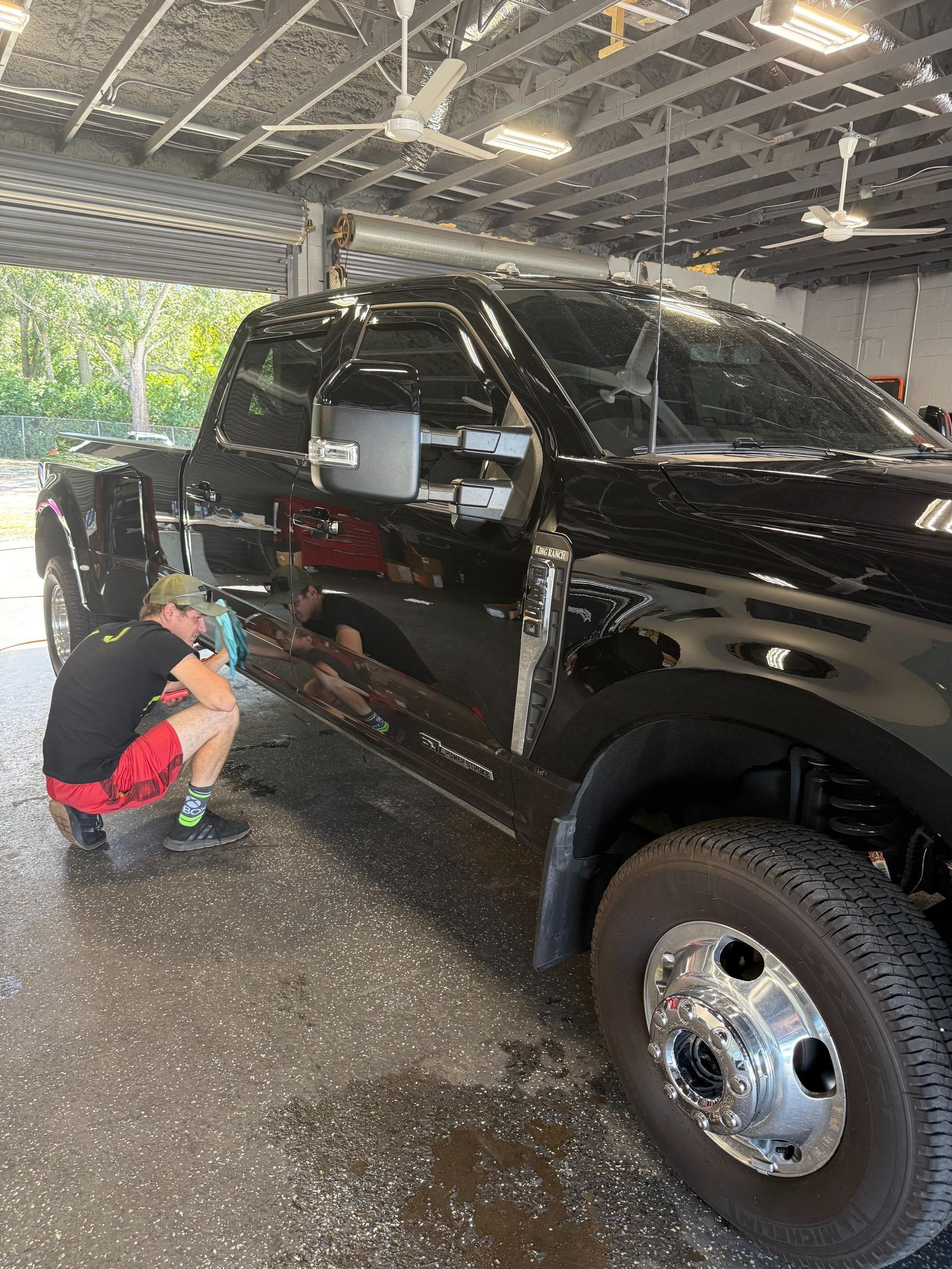 Person washing a black pickup truck at a car wash. They are spraying the side of the truck.