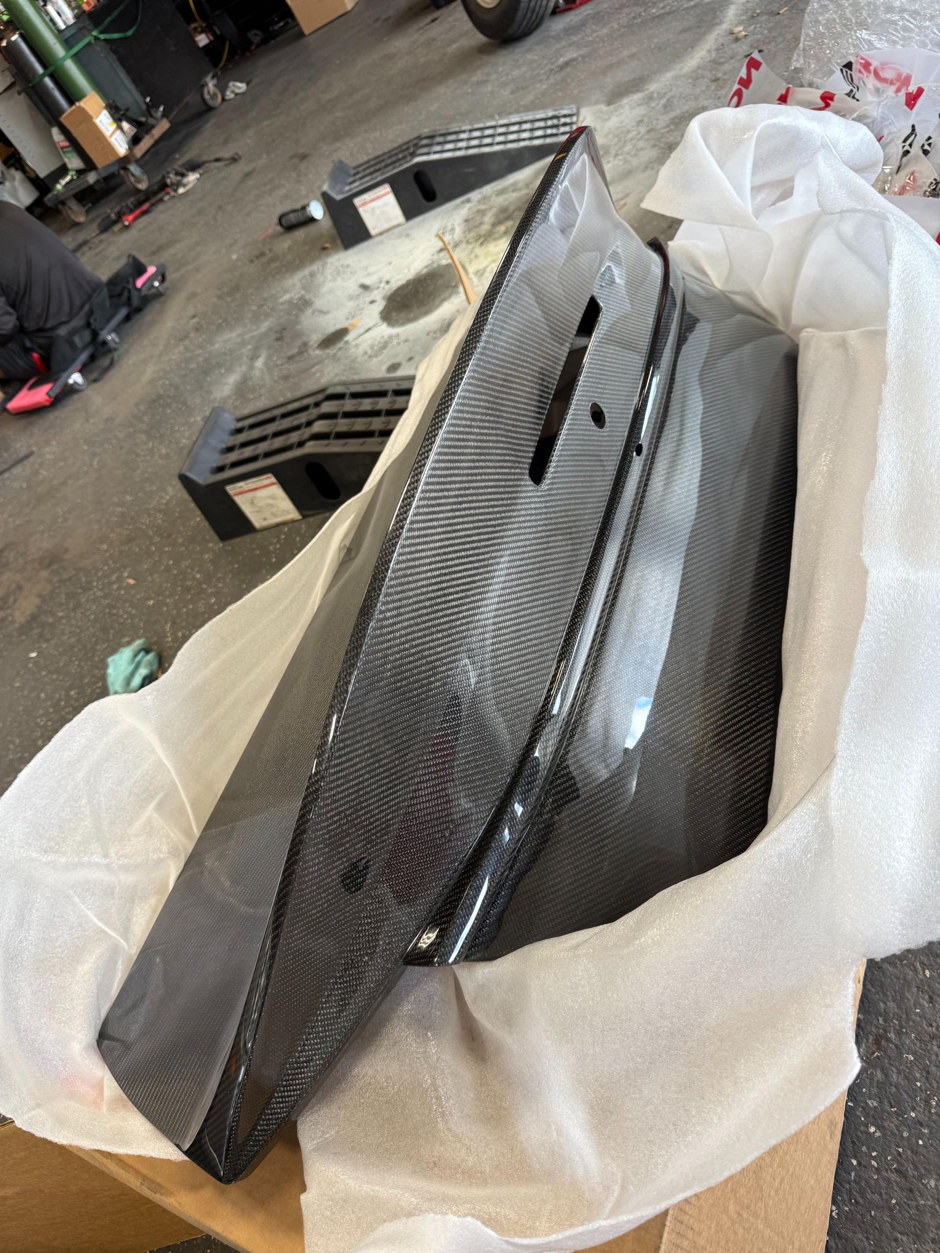 Carbon fiber car panels, wrapped in protective white foam, in a garage setting.