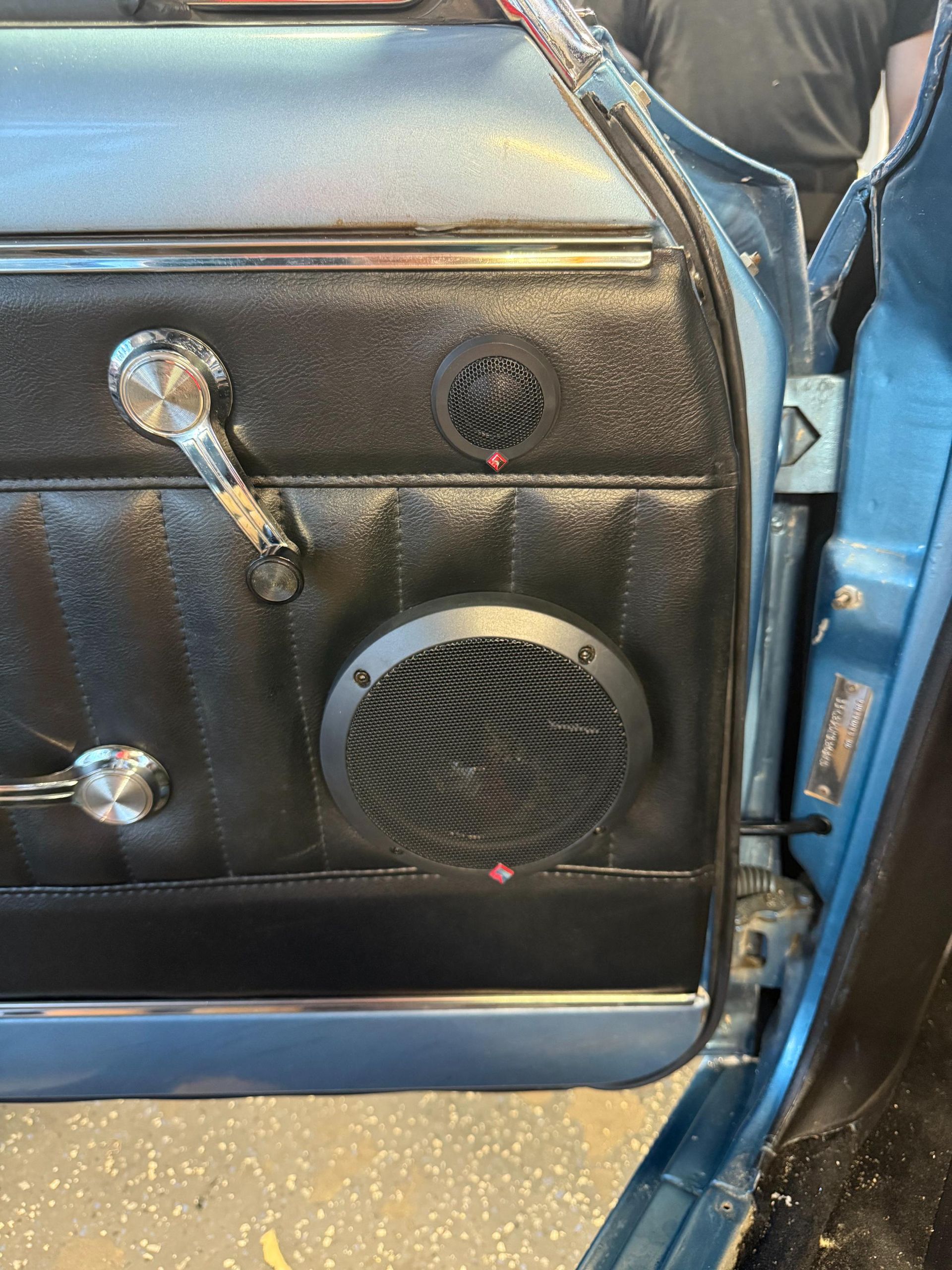 Car door panel with speaker grilles installed. Black panel, chrome handles, blue car frame.