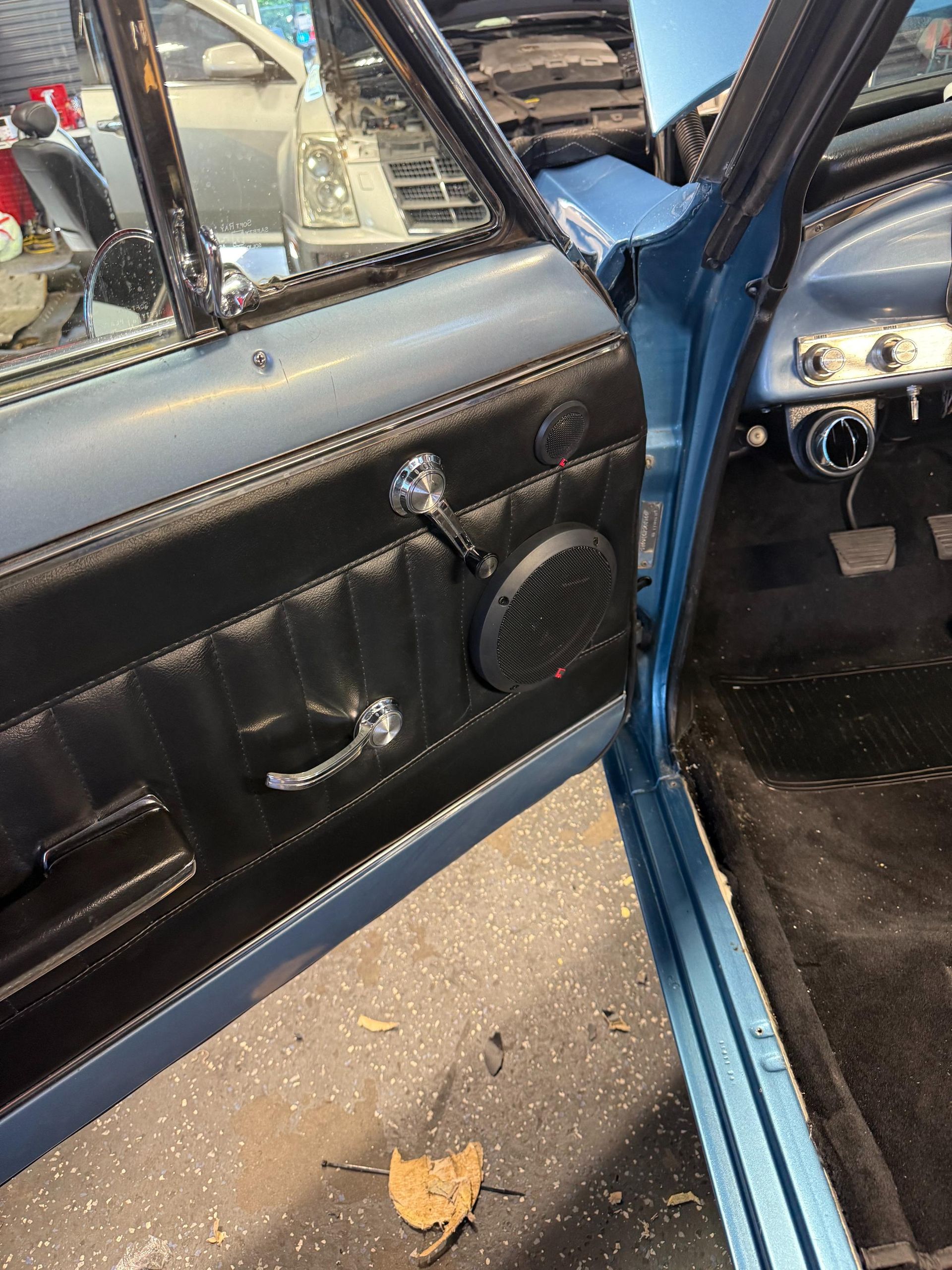 Blue car door open; black panel with speaker, chrome handles. Interior view.