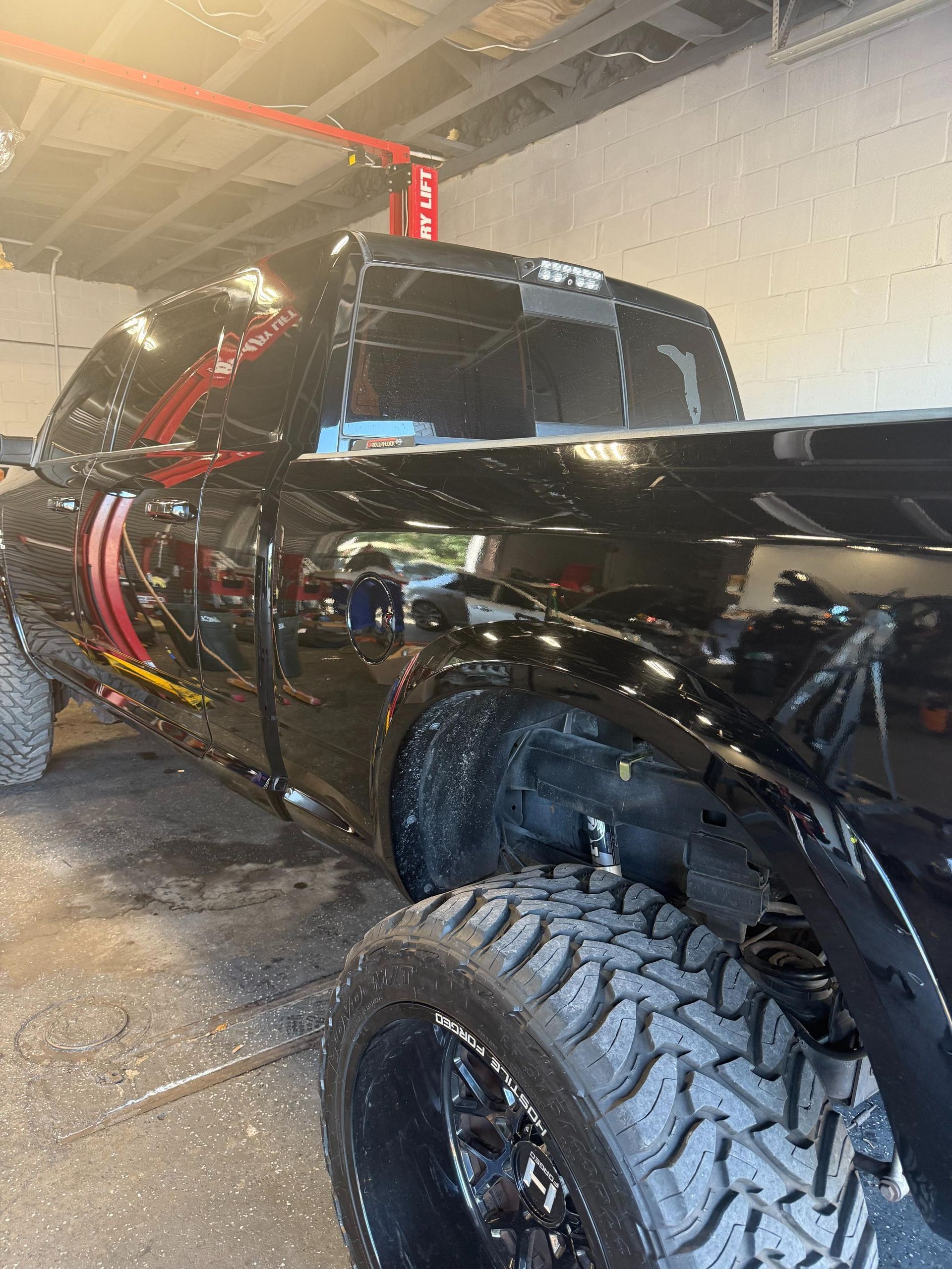 Black truck with large tires being washed inside a garage.