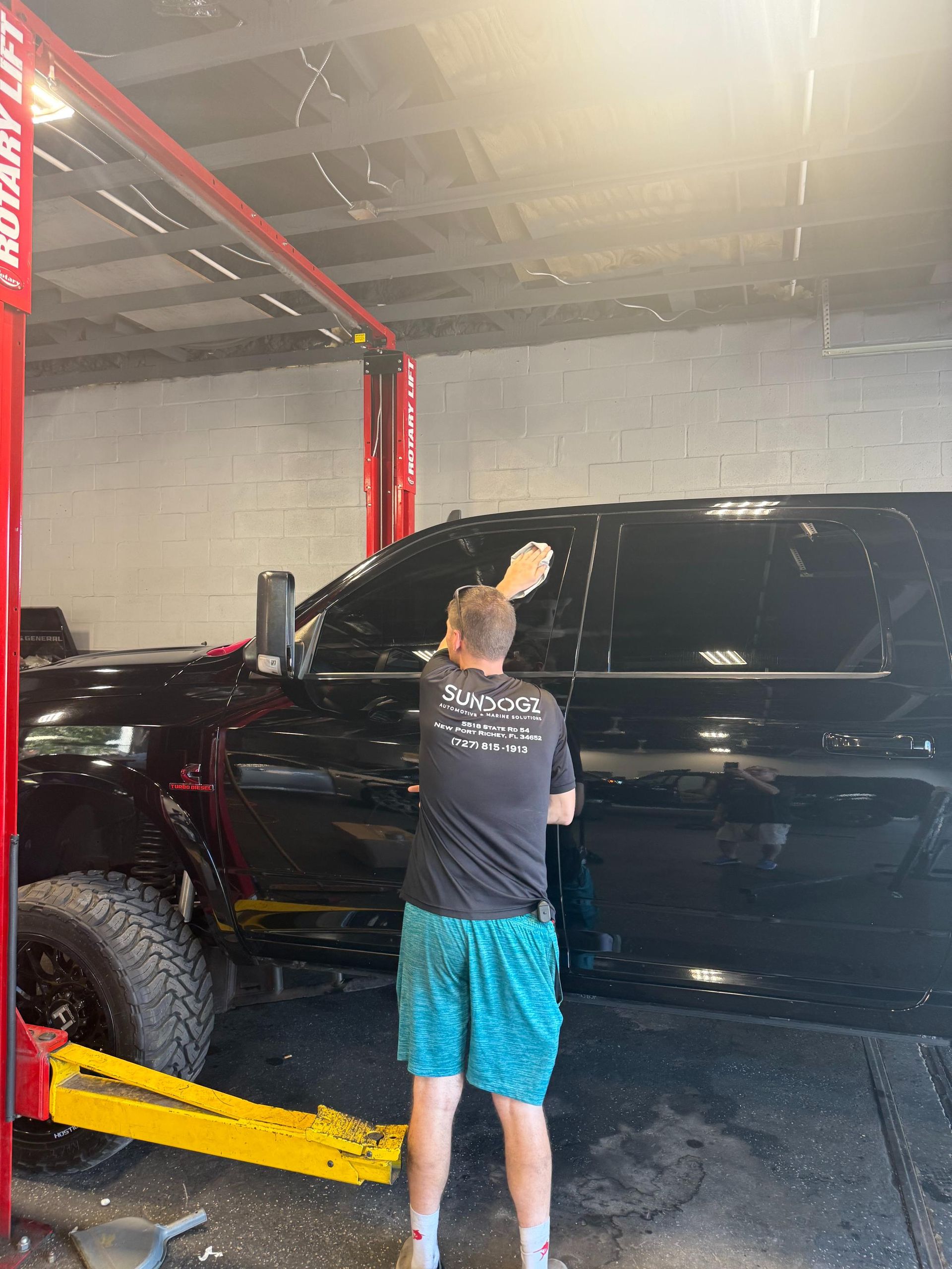 Person washing a black truck window inside a garage with a red car lift.