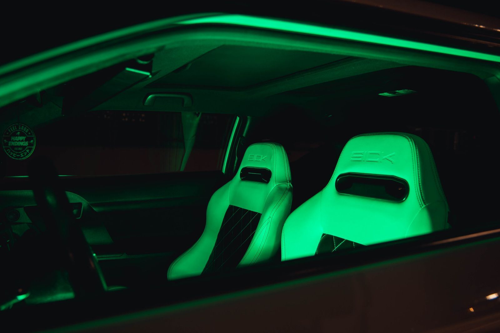 Car interior with green neon light illuminating white seats.