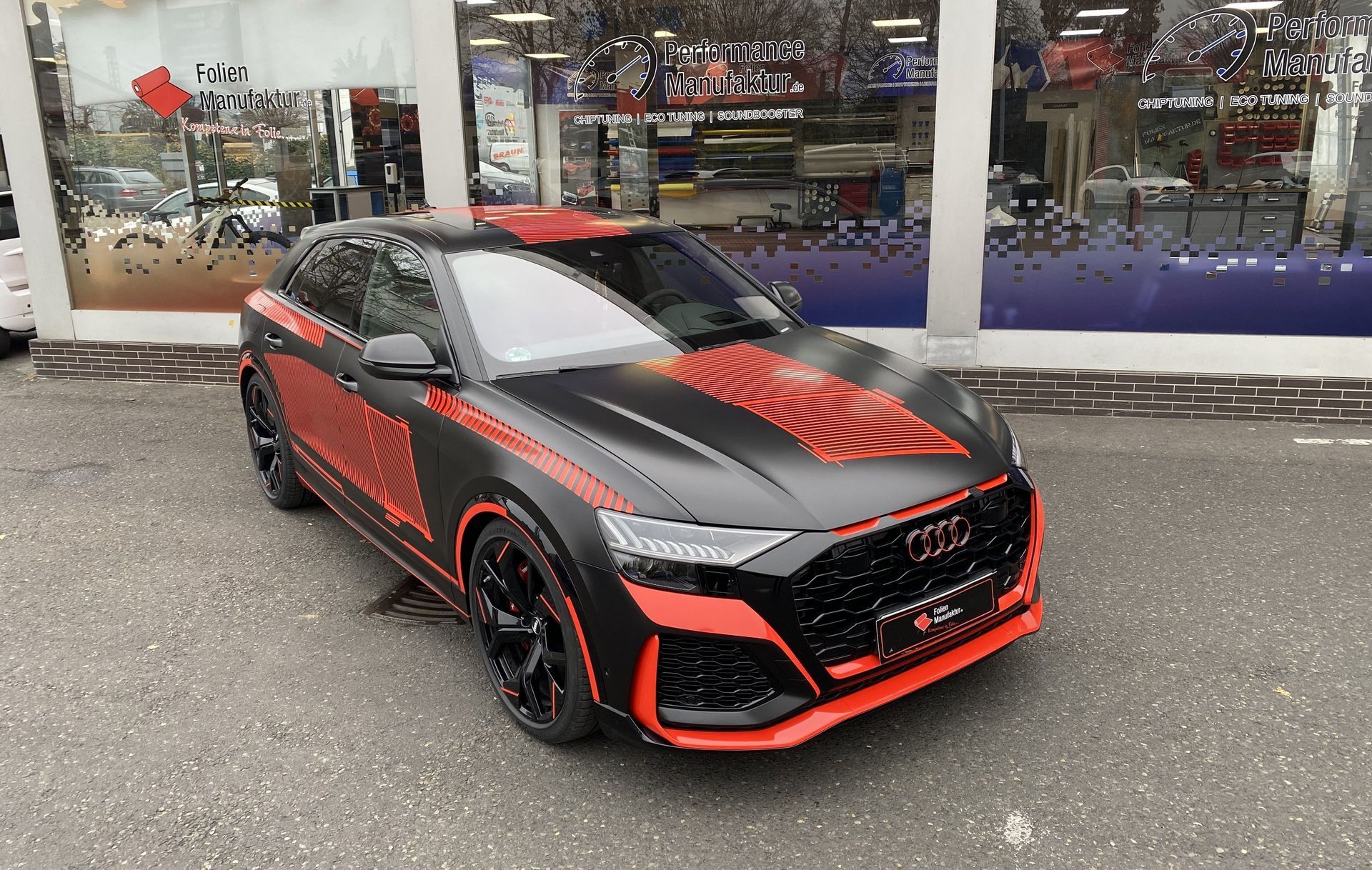 Black and red Audi SUV parked in front of a shop; custom paint job.