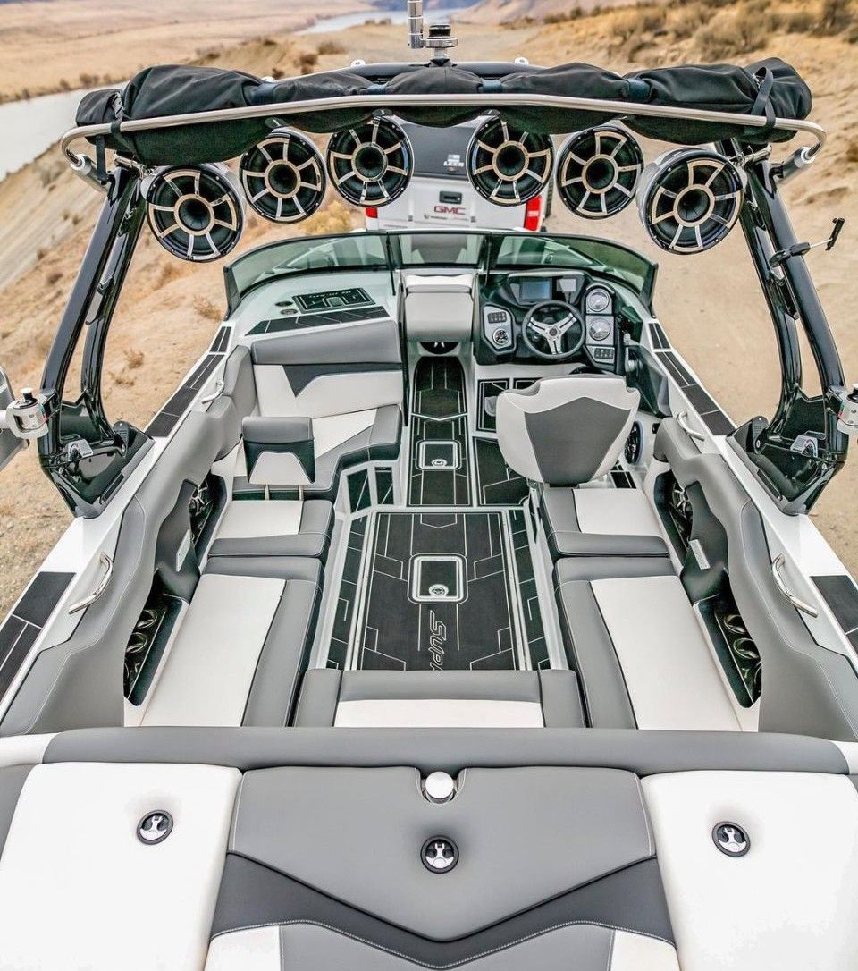 Interior of a white and gray luxury motorboat with multiple speakers, a helm, and cushioned seating.