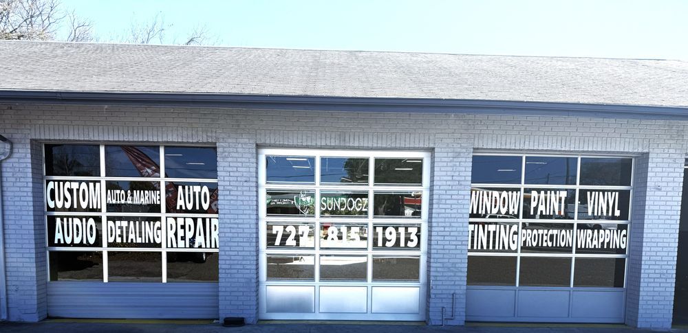 Garage with services listed on the windows: custom audio, detailing, repair, window paint, and vinyl. Phone number displayed.