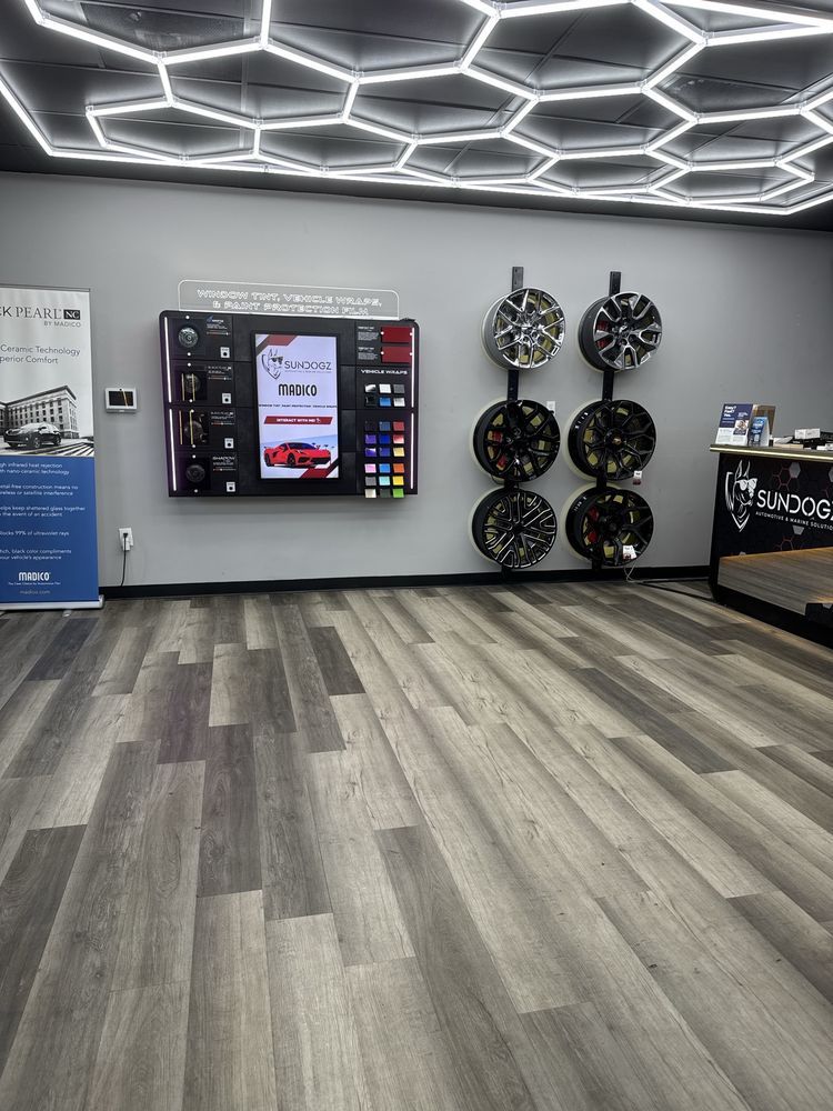 Interior of a store displaying wheels, a touch screen, and hexagon-shaped ceiling lights. Wooden floor.