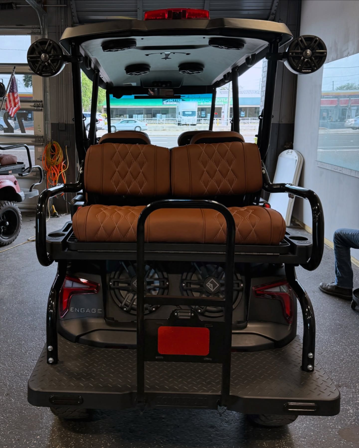 Rear view of a custom golf cart with brown diamond-stitched seats, black frame, and exterior speakers.