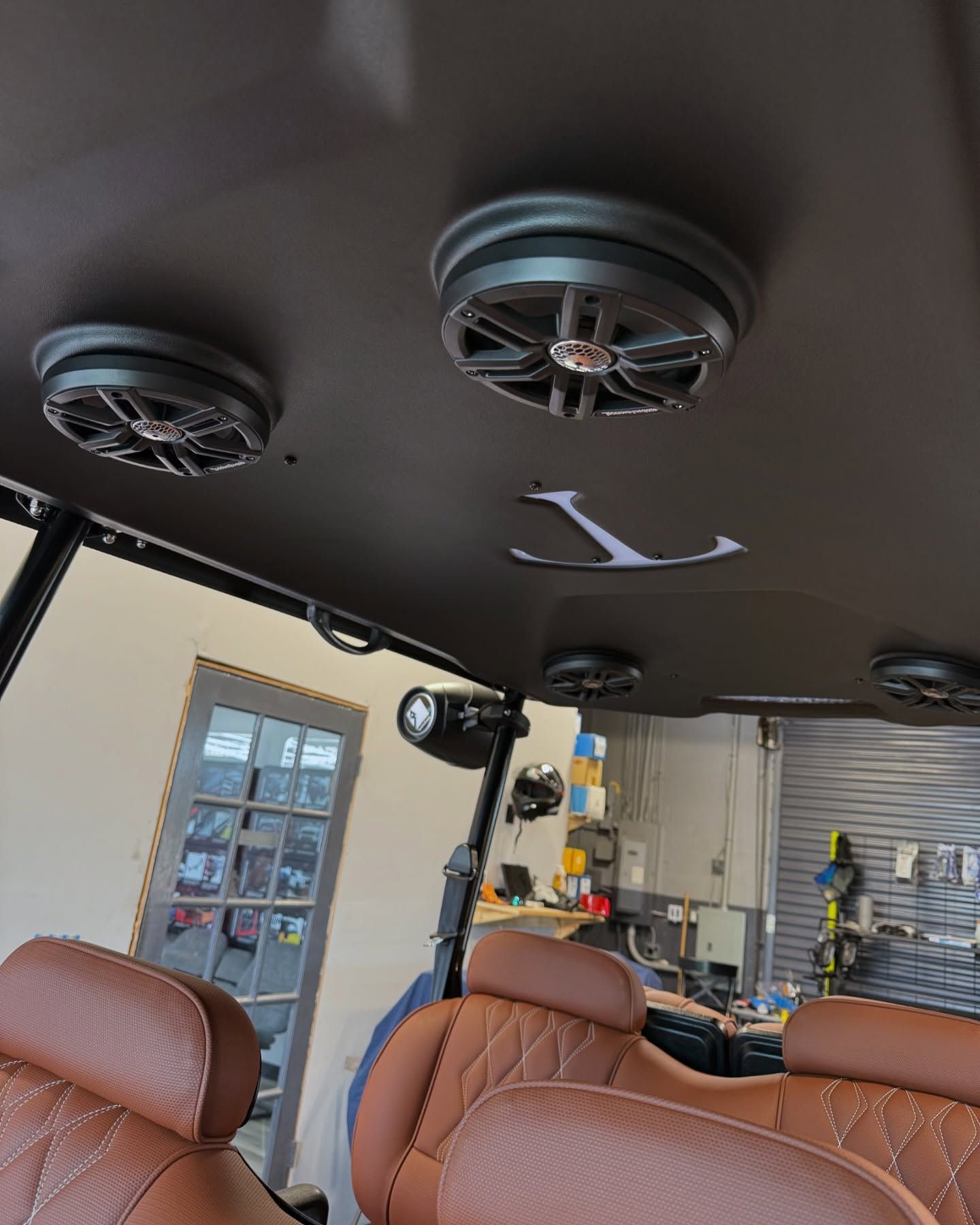 Brown interior of a golf cart with speakers, brown seats, and an anchor cutout on the ceiling.