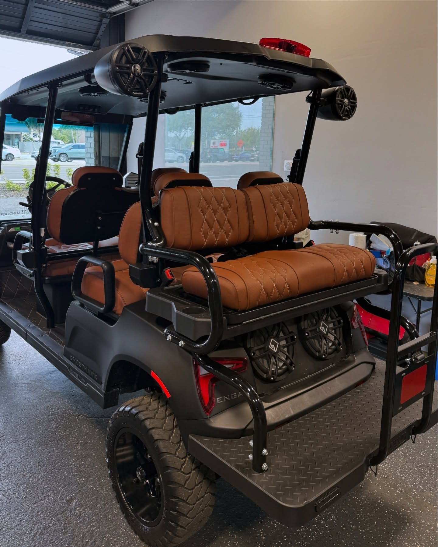 Black and brown golf cart with speakers and plush seating, parked indoors.