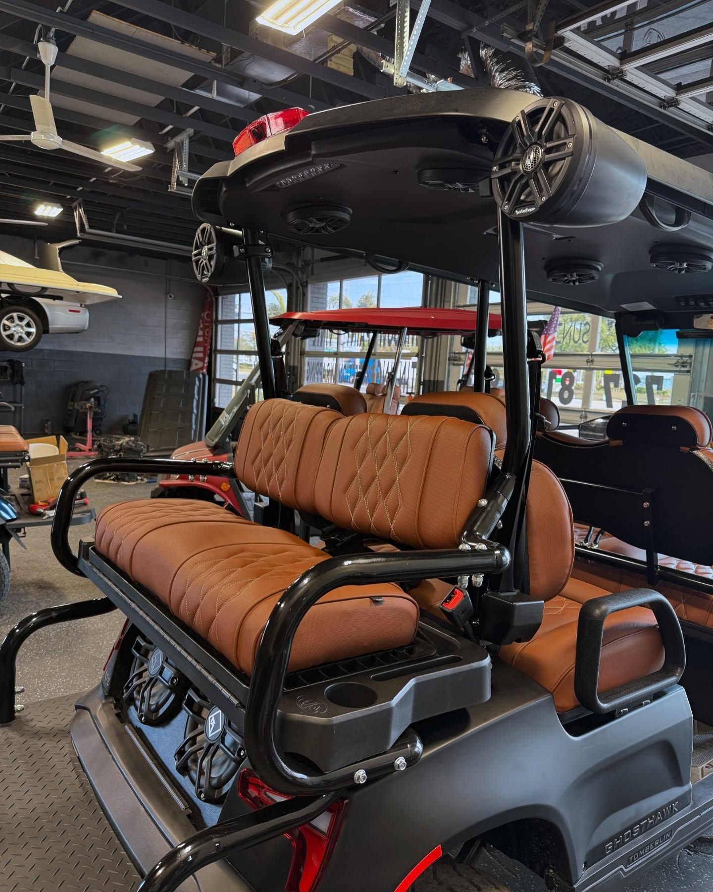 Brown leather seats on a custom golf cart. Black frame, black roof with speakers. Inside a shop.