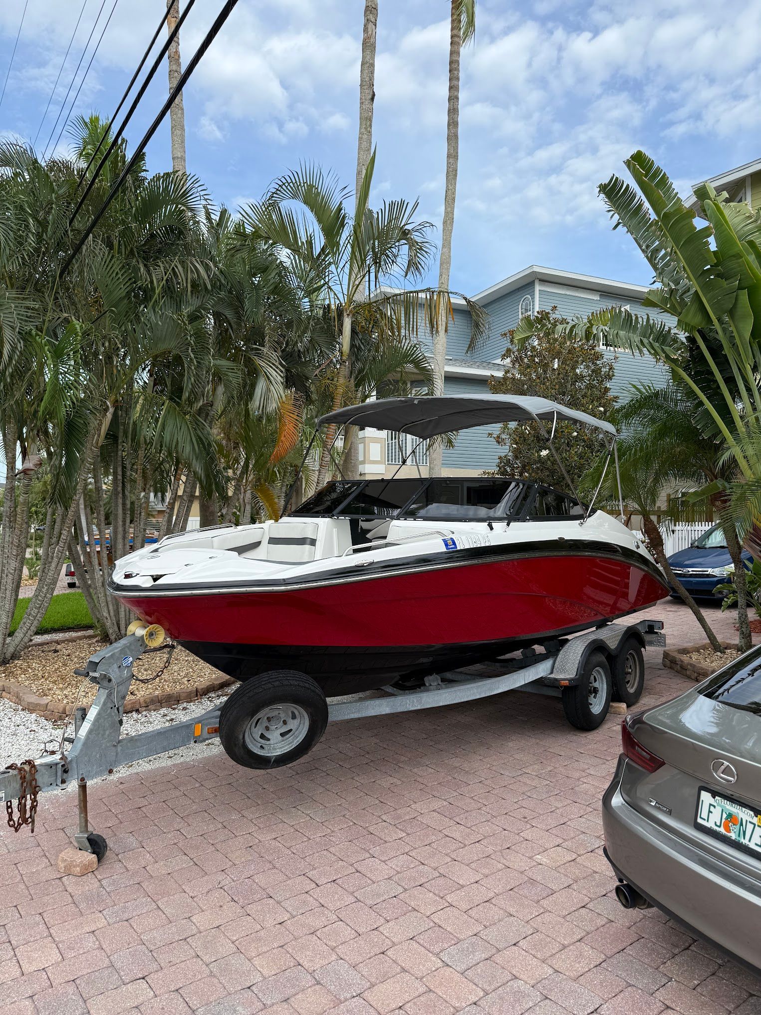 Red and white motorboat on trailer, parked on a brick driveway, with a canopy.