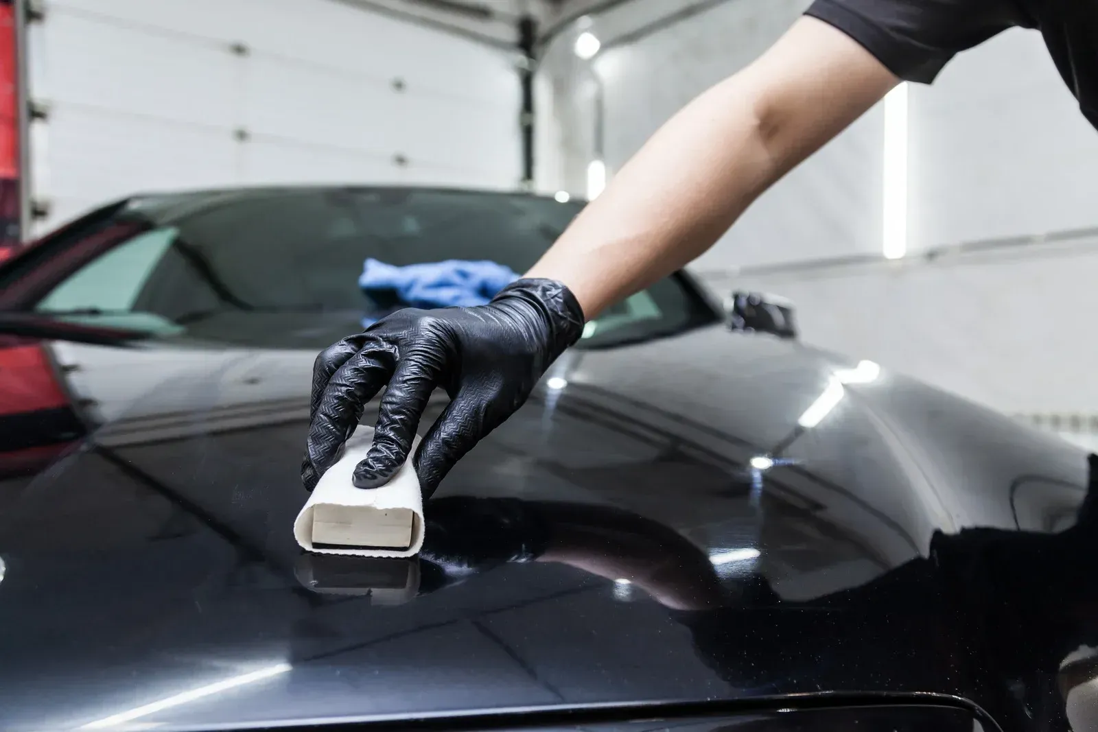 Person wearing black gloves applying ceramic coating to a black car.