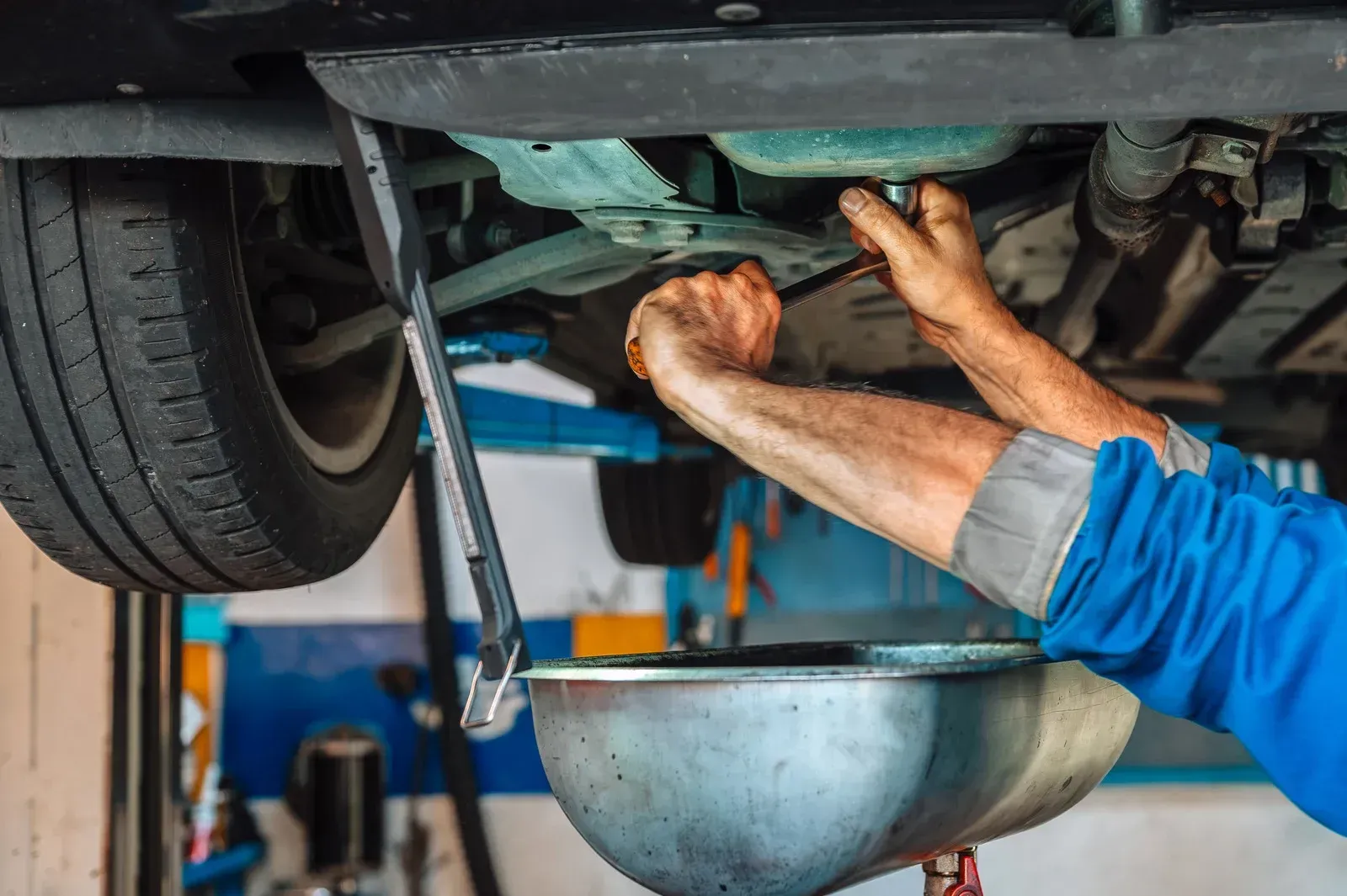 Mechanic changing oil under a car in a garage, using a wrench.