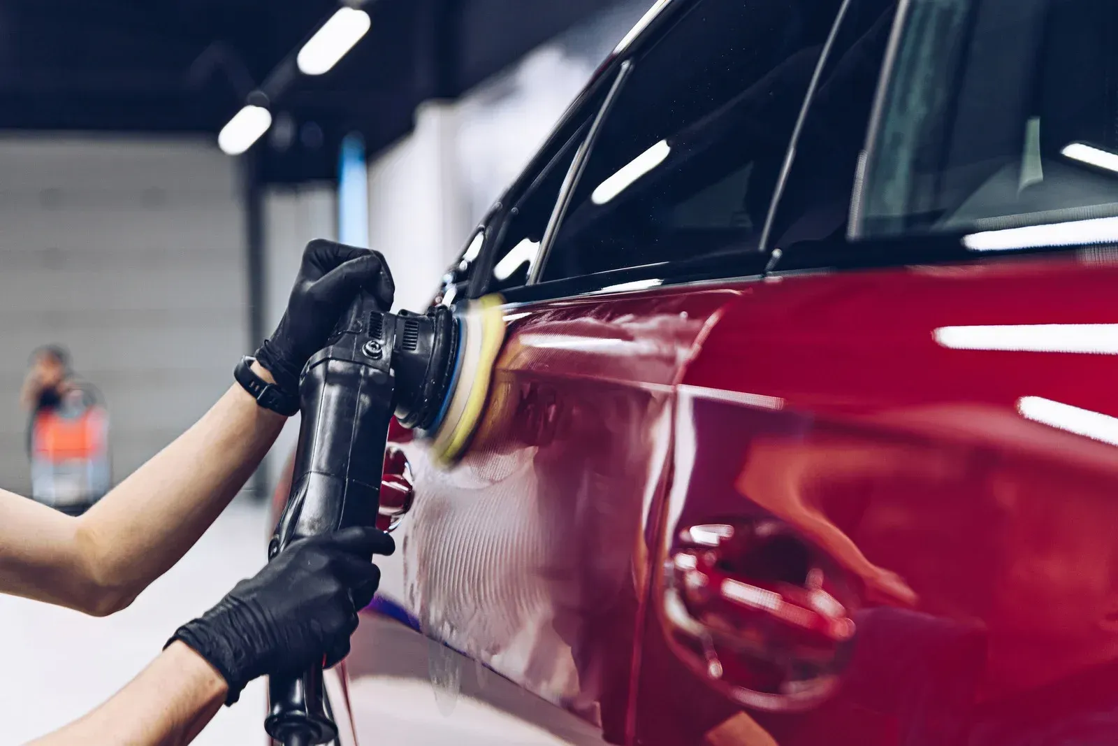 Person polishing a red car with a power buffer in a garage.