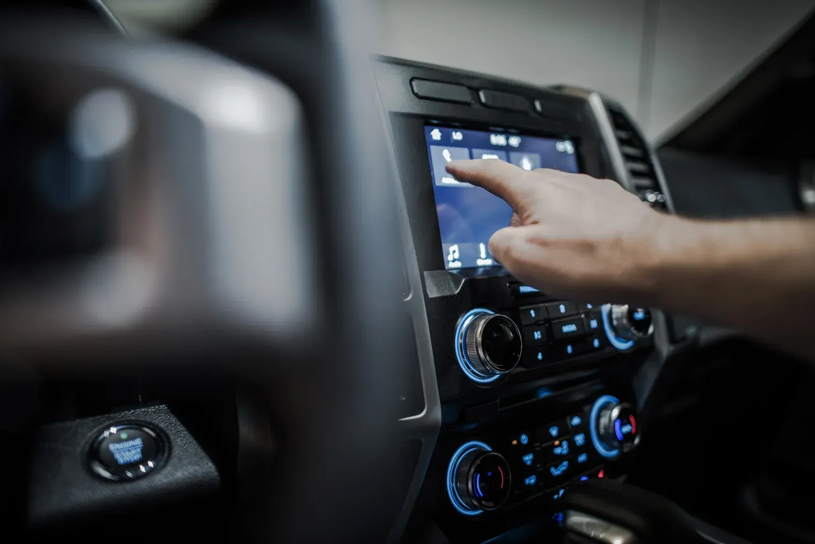 Hand pointing at touchscreen interface in a car's dashboard.
