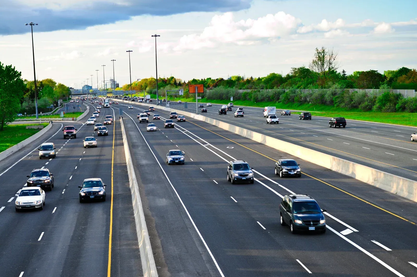 Cars traveling on a multilane highway, with trees and a cloudy sky in the background.