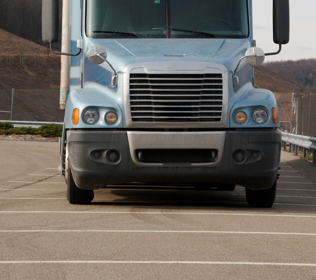 Blue semi-truck parked in a paved lot. Front view with a mountain in the background.