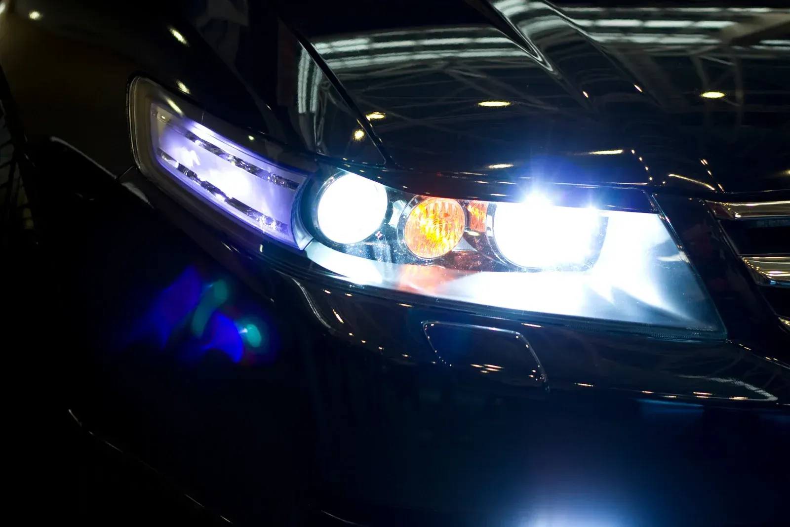 Close-up of a black car's headlight illuminated with bright white and purple lights.