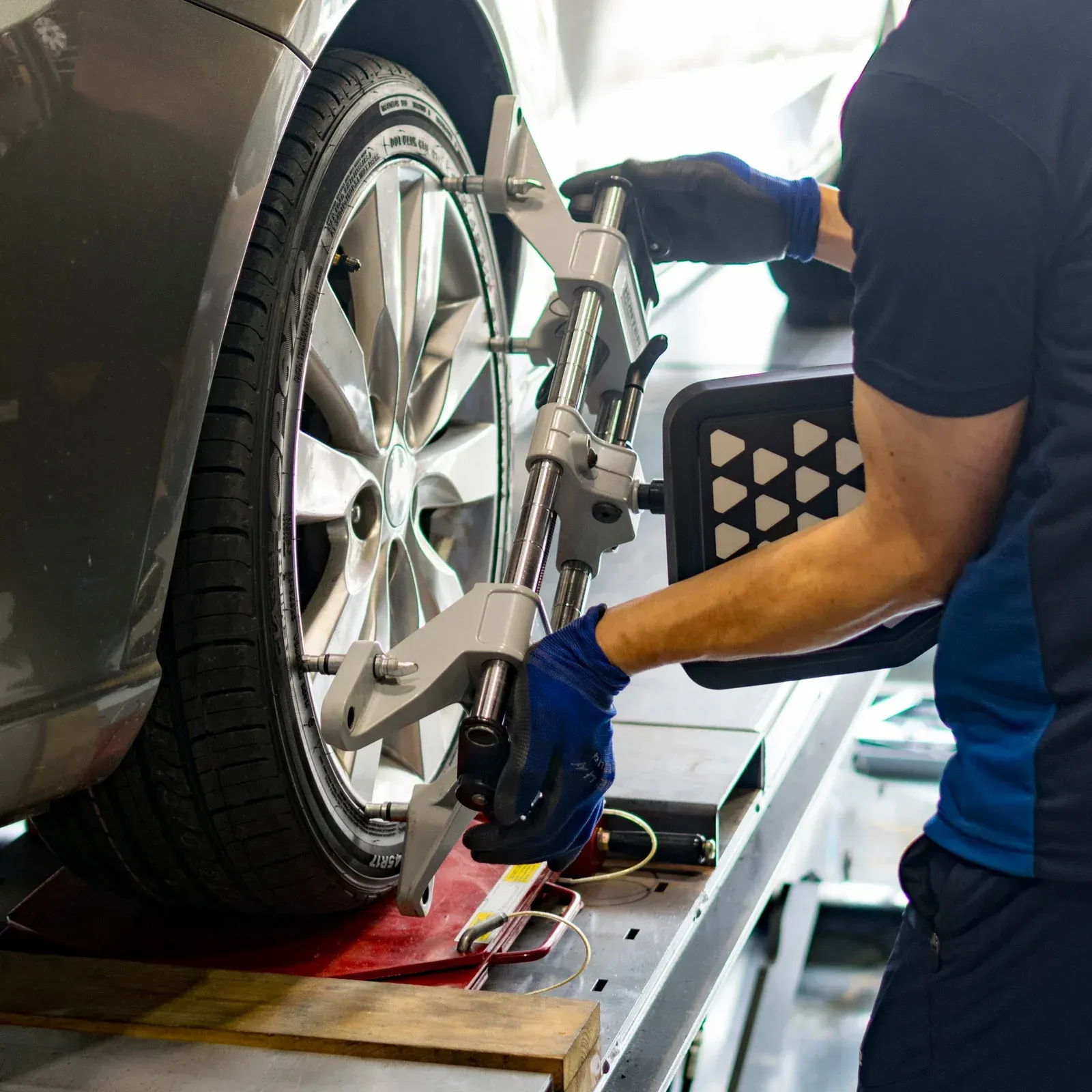 Mechanic using alignment tools on a car tire in a garage, wearing blue gloves.