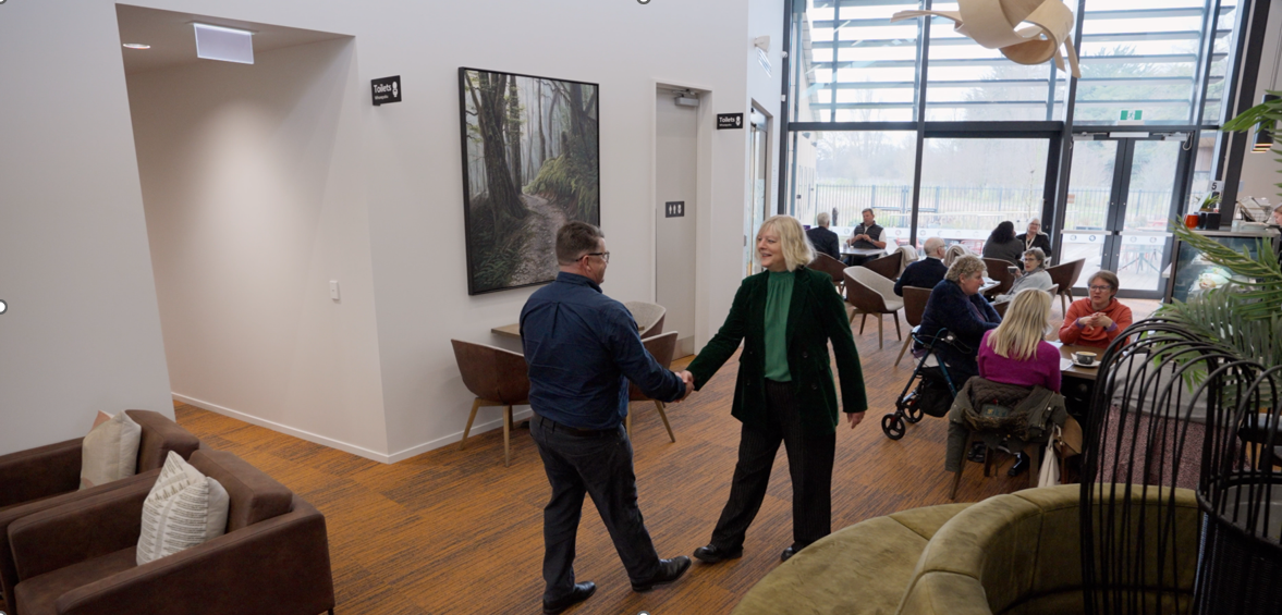 Rex Prebble of Christchurch Electrical and Leesa Loffhagen of The BrainTree Wellness Centre shaking hands in the centre with customers in the cafe.