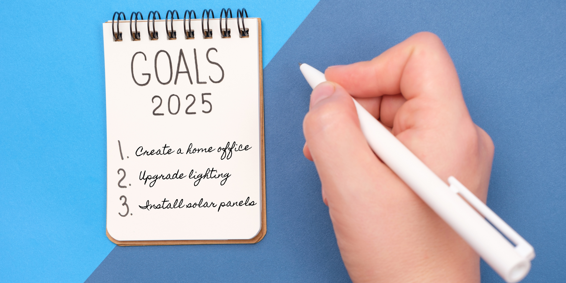 Notepad with list and hand with pen: Goals 2025, 1. Create a home office 2. Upgrade lighting 3.  Install solar panels