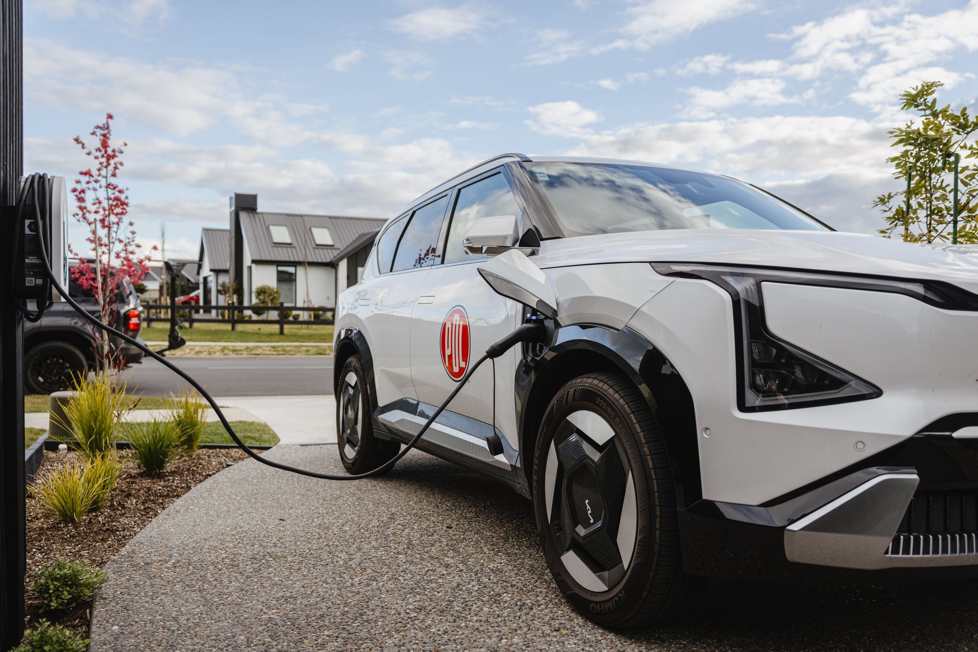 White car on driveway plugged into an EV charger.