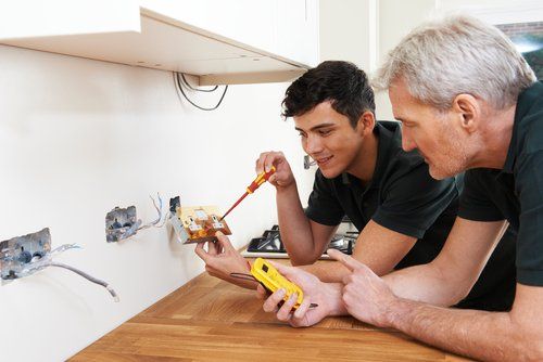 Two men with tools looking at a power socket