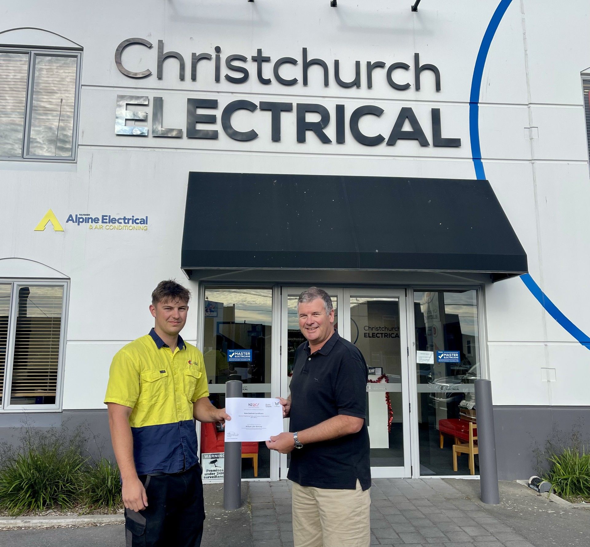 William Bentley receiving certificate from Warren Bentley outside of Christchurch Electrical's office.