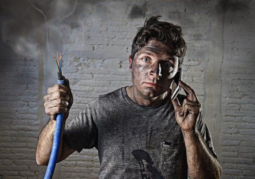 A person holding a smoking electrical wire and a phone against their ear