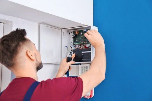 An electrician installing a security system next to a blue wall