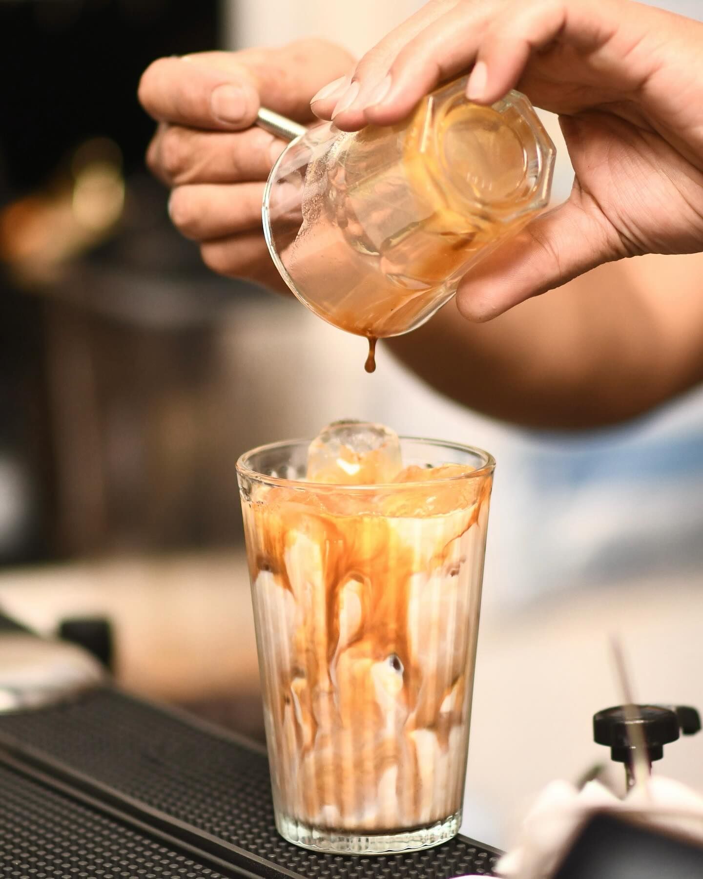 Barista pouring caramel over iced coffee in a glass, creating a layered effect.