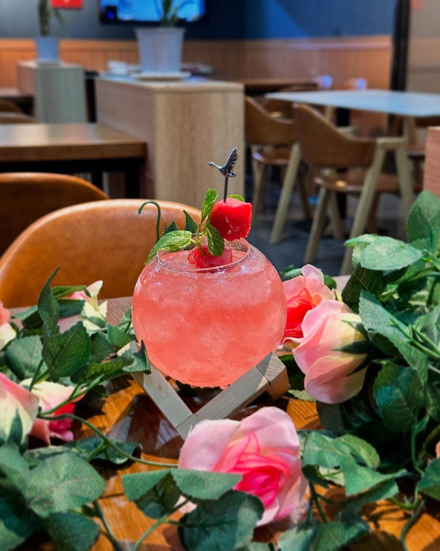 A pink drink with a cherry on top is sitting on a table surrounded by flowers.