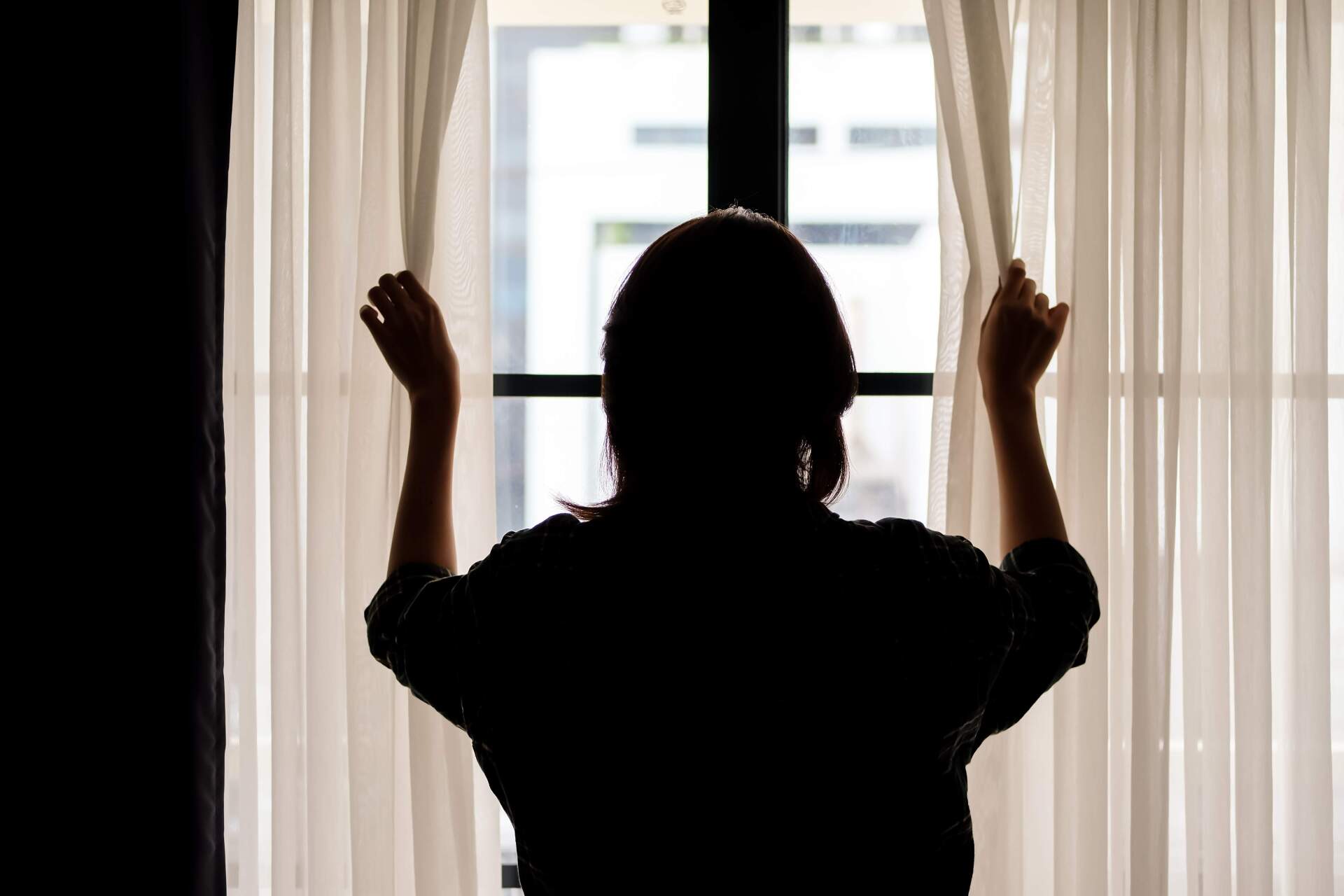 Woman opening white sheer curtains to city view at Belamy House Makati